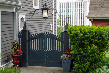 A black wooden gate with decorative palings and posts. A vintage wrought iron lantern hangs over...