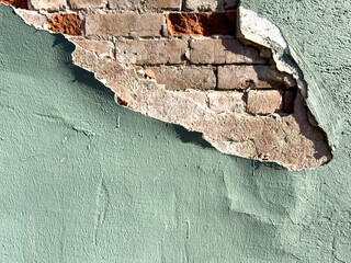 A thick layer of stucco on the outside of a brick building. The exterior wall is made of red brick. The plastered coating of the wall is a textured waterproofing. The brick is damaged and eroding. 
