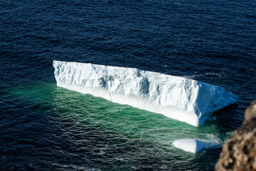 A large white iceberg formation floating in the cold ocean with layers of textured ice and snow....