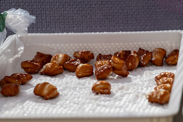 A large white plastic tray and liner filled with fresh soft pretzel bites. The sweet bread is coated in butter and sprinkled with sea salt. The mini pretzels have a dark brown outer crust. 