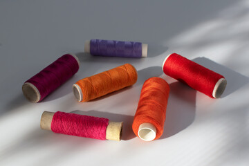 Multicolored spools of sewing thread, closeup. Colored threads on a white background in sunlight