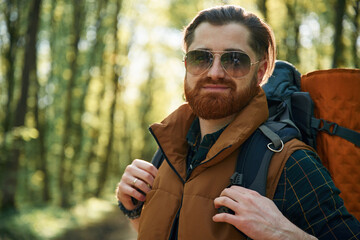 In cool sunglasses. Bearded man is in the forest at daytime