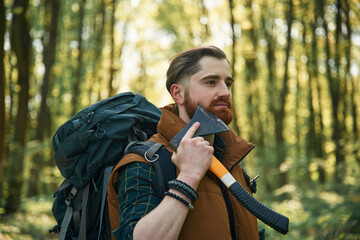 Shaving by using an axe. Bearded man is in the forest at daytime