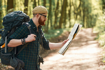 Focused on reading the map. Bearded man is in the forest at daytime