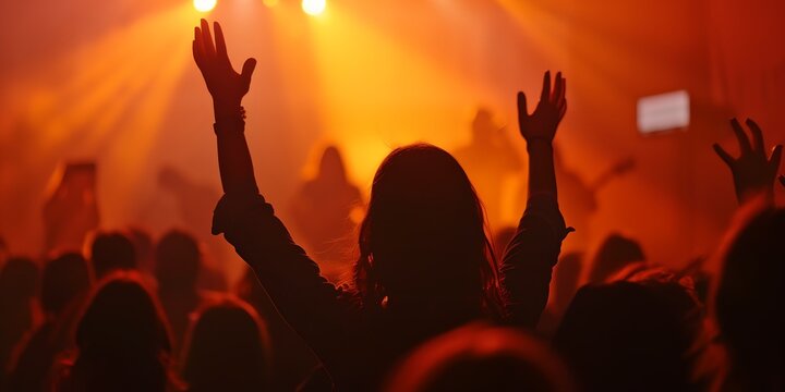 a woman raising her hands in the air at a concert with a crowd of people in the background at night.