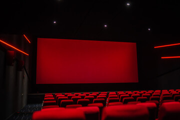 An empty movie theater with rows of red seats facing a large red screen, bathed in a moody red...