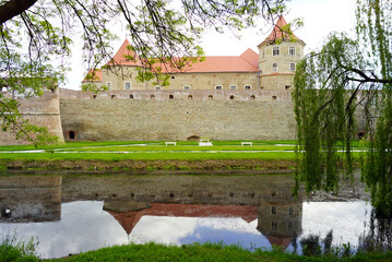 View of the Fagaras fortress in Romania: a landscape with a water-filled moat, trees, a defensive...