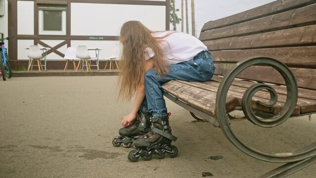 Close up little girl in a park tying or putting on the rollerblade inline, preparing to skate, tying laces and straps while on a bench outdoors