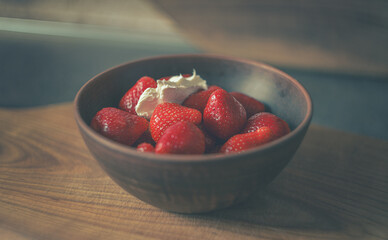 Home kitchen. Strawberries with cream in a clay plate on a wooden board