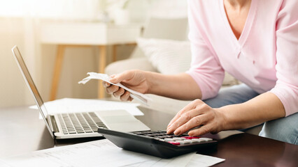 Cropped of woman is seated at a desk, focused on her work. She is using a calculator and a laptop to perform financial calculations or analysis. The setting is a typical office environment.