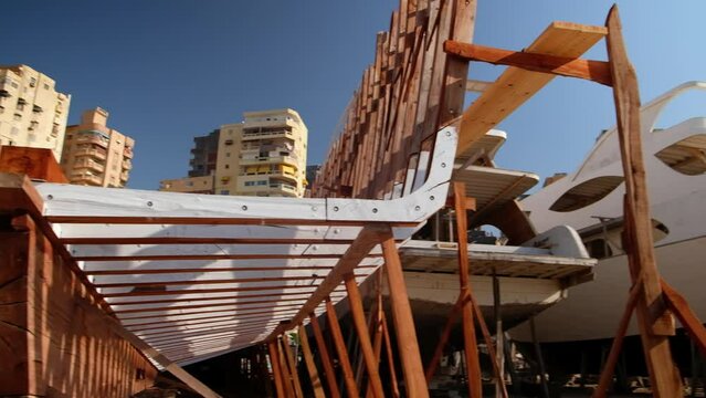 Craft shipyard. Hull of yacht at wharf under construction. Low angle view of yacht frame on a stock. Wooden vessel being constructed