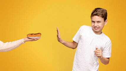 A young boy with a disgusted expression declining a hotdog from an outstretched hand.
