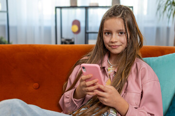 Young girl texting share messages content on smartphone social media applications online watching relax movie. Female Caucasian teenager kid child uses mobile phone sits on sofa in living room at home