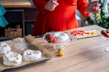 Two chefs in a vibrant kitchen collaborate on decorating a pavlova with fresh strawberries and...