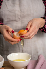 Close up of hands skillfully cracking an egg, the yolk separating from the white into a bowl, a fundamental technique in culinary preparation.