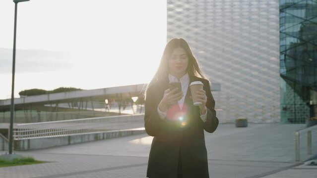 Young businesswoman in a black suit looking at her phone in front of office buildings 
