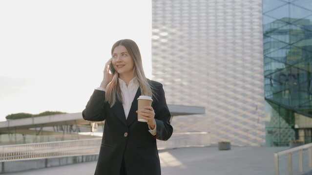 Young businesswoman in a black suit talking on the phone while holding a cup of coffee