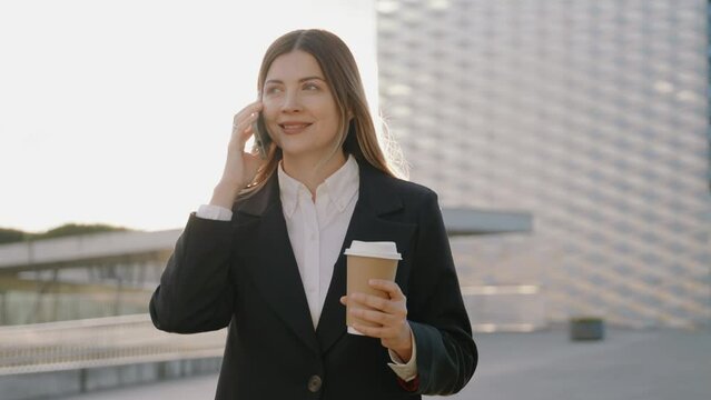 Young businesswoman in a black suit talking on the phone while holding a cup of coffee