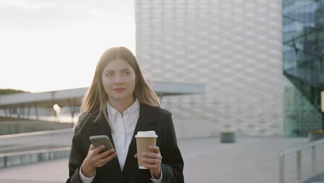 Young businesswoman in a black suit looking at her phone in front of office buildings 
