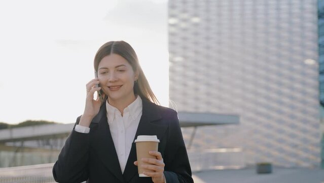 Young businesswoman in a black suit talking on the phone while holding a cup of coffee