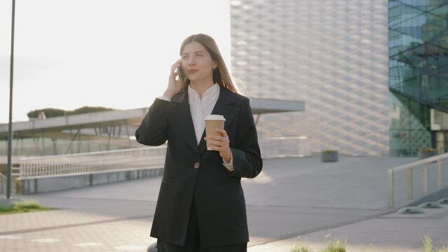Young businesswoman in a black suit talking on the phone while holding a cup of coffee
