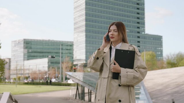 Young businesswoman in a black suit talking on the phone while holding a folder