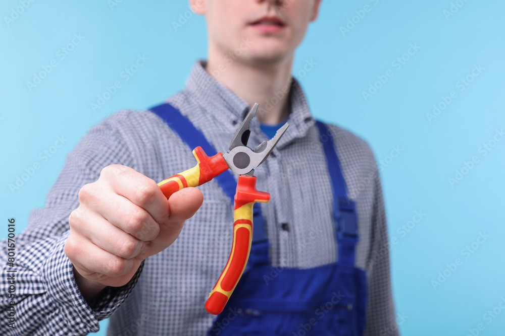 Sticker Young man holding pliers on light blue background, closeup