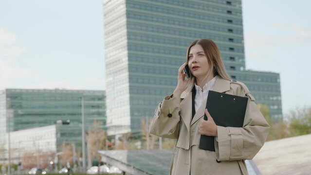 Young businesswoman in a black suit talking on the phone holding a folder