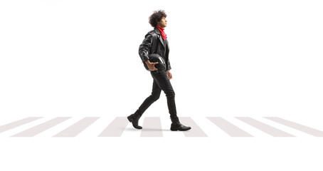 Full length profile shot of a of a young man in leather jacket walking at a pedestrian and carrying...