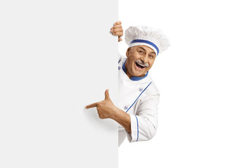 Mature male chef in a uniform pointing and standing behind a blank panel