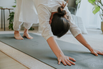 an asian woman wearing loosing white clothes doing downward facing dog pose, yoga at home