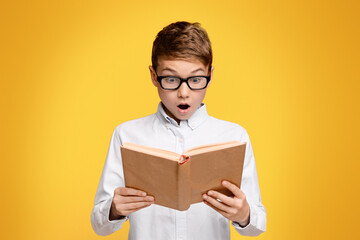 A young boy with glasses engrossed in reading a book.