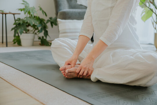 an asian woman wearing loosing white clothes doing bound angle pose, yoga at home