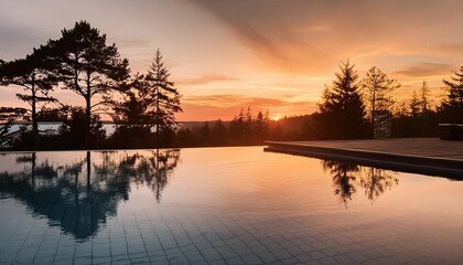a pool with a view of trees and a sunset the water is calm and the sky is orange