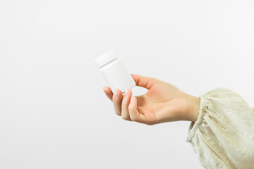 hand holding a white plastic jar with pills on a white background. health care concept