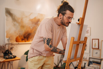 Focused creative artist painting on easel at artistic studio.
