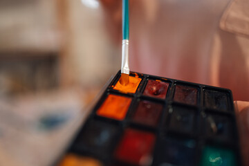 Close up of paintbrush mixing watercolor palette in art studio.