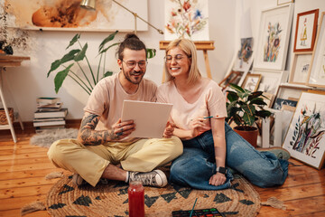Creative artist couple sitting on floor at studio and looking at artwork