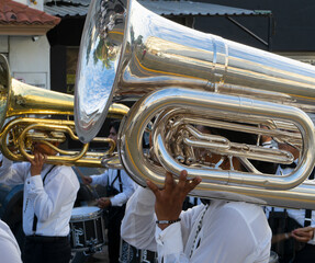 Close-up of a polished brass tuba with musician's hands, white-shirted band members in the background, during an urban parade in Cancun, Mexico