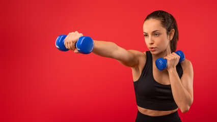 Closeup of beautiful young woman with long hair holding two blue dumbbells in her hands, showcasing her strength and fitness regimen