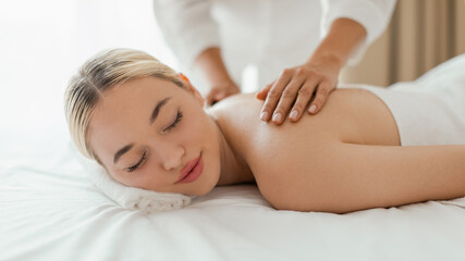 A woman lying face down on a massage table at a spa, receiving a back massage from a massage...