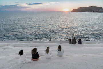 des personnes assises sur des rochers blancs face à un coucher de soleil sur la mer