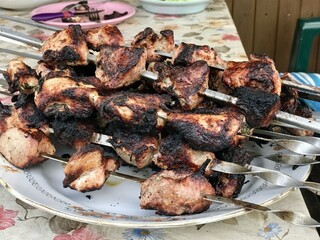 Overcooked meat on metal skewers after coals in the grill lies on a white plate on the table. Spoiled meat during cooking outdoors. Close-up