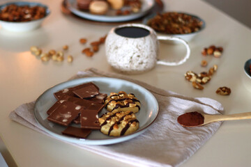 Cup of tea or coffee, cookies, macaroons, chocolate, various nuts and cocoa powder on white background. Selective focus.
