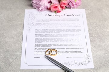 Marriage contract, golden wedding rings, pen and flowers on grey table