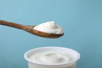 Eating delicious natural yogurt on light blue background