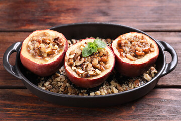 Tasty baked apples with nuts, honey and mint in baking dish on wooden table, closeup