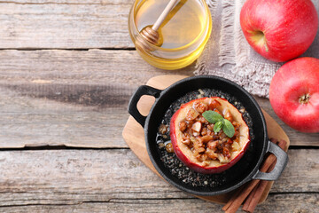 Tasty baked apple with nuts in baking dish, honey and cinnamon sticks on wooden table, flat lay....