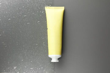 Tube with moisturizing cream on wet grey surface, top view
