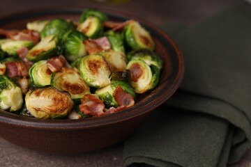 Delicious roasted Brussels sprouts and bacon in bowl on brown table, closeup